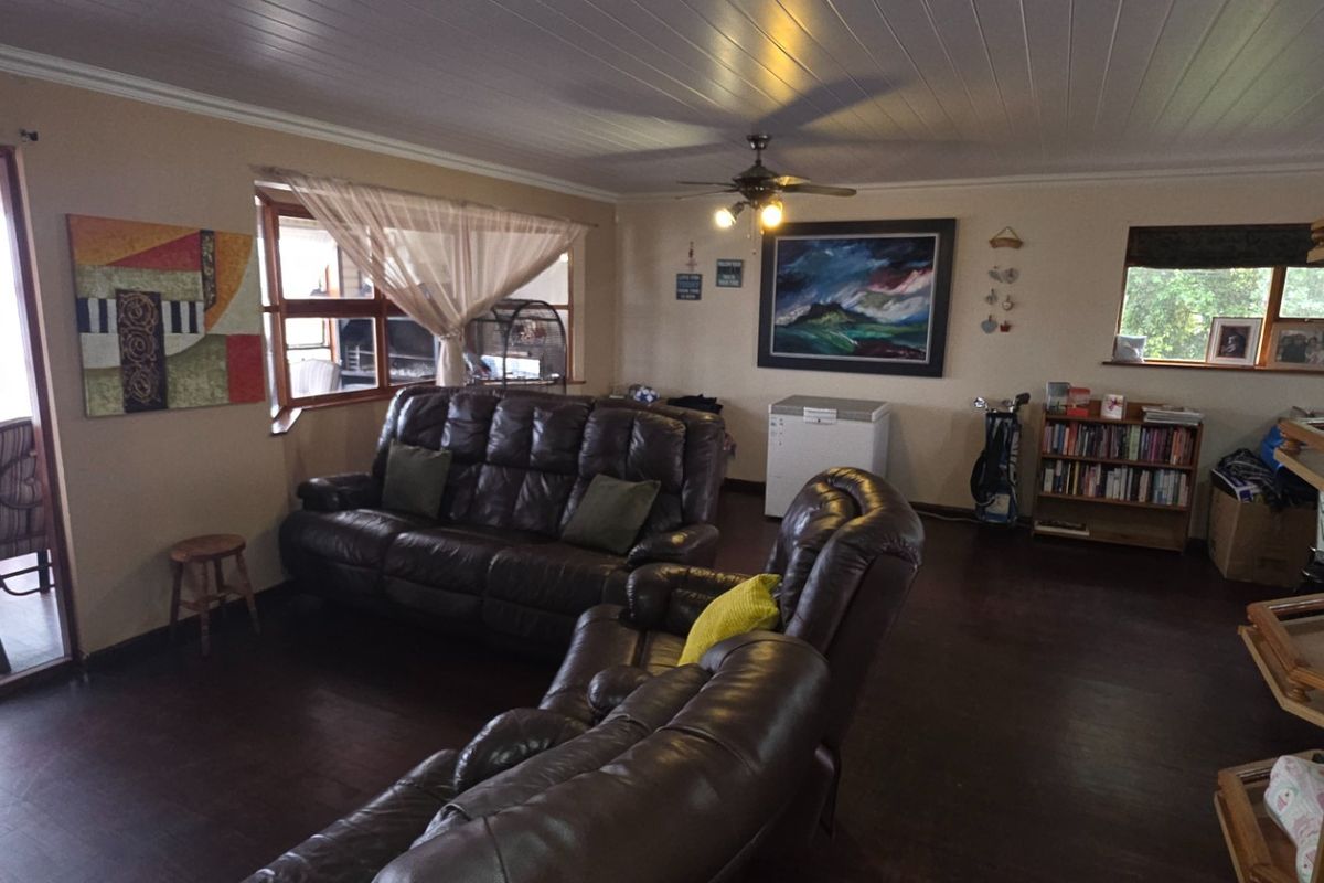 Spacious living area featuring timber-look flooring, a panelled ceiling with a central fan, and direct access to an adjoining patio through sliding glass doors.