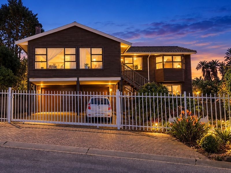 A well-maintained two-story timber-clad house featuring a paved driveway, secure metal fencing, and an integrated double garage at twilight.