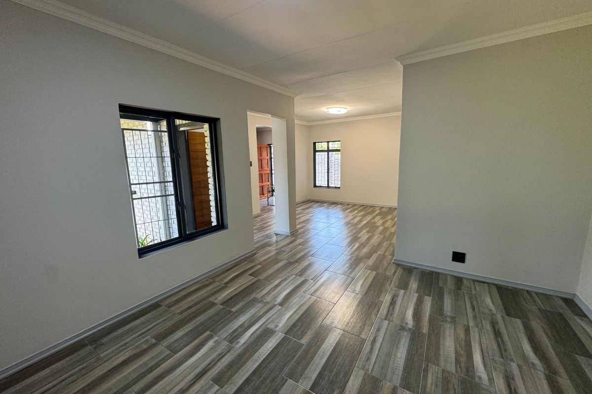 A bright, empty living area featuring modern wood-look tiled flooring, neutral walls, and security bars on the windows.
