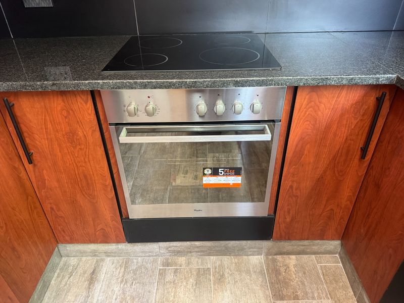 A well-maintained kitchen section featuring a built-in stainless steel oven, electric hob, granite countertops, and warm-toned wooden cabinetry.