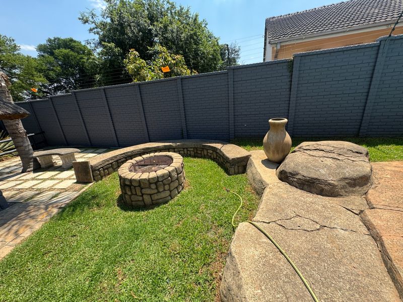 A landscaped garden area featuring a stone fire pit, curved stone seating, paved patio space, and a secure brick boundary wall with electric fencing.