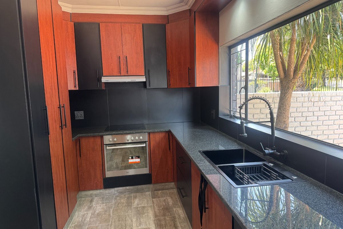 Modern kitchen featuring two-tone cabinetry, granite countertops, integrated electric oven and hob, and a large window overlooking the garden.