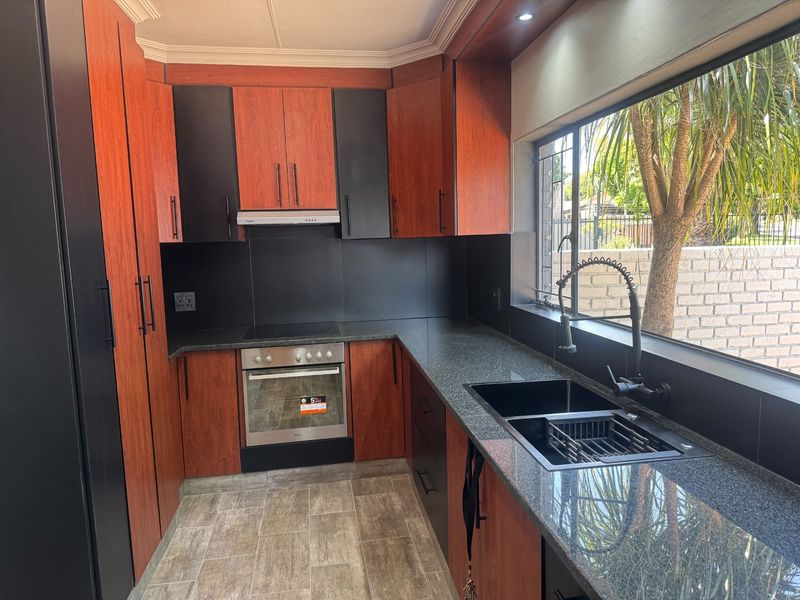 Modern kitchen featuring two-tone cabinetry, granite countertops, integrated electric oven and hob, and a large window overlooking the garden.