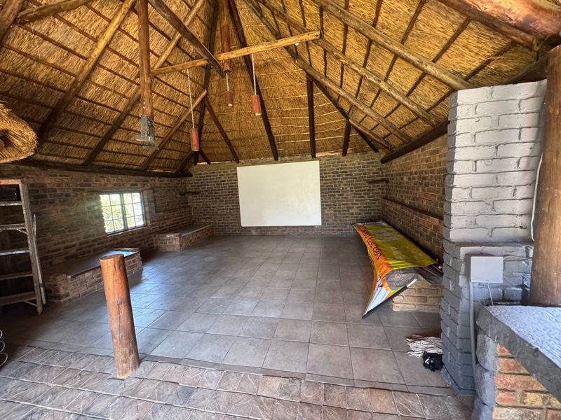 Spacious covered outdoor entertainment area featuring a traditional thatched roof, exposed brick walls, tiled flooring, and built-in brick seating with a fireplace.