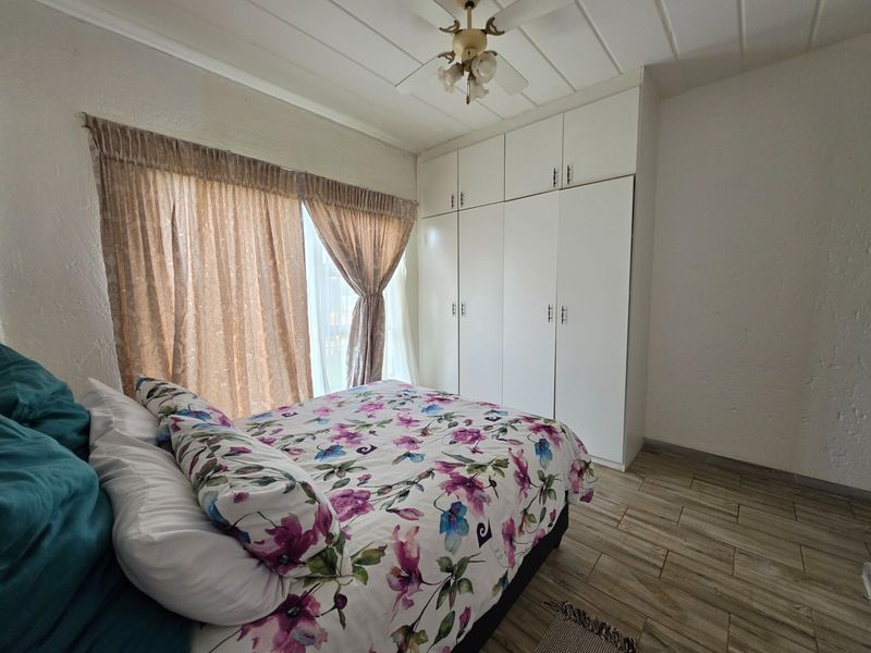 A bedroom featuring built-in cupboards, a ceiling fan, and tiled flooring, offering a functional space with neutral finishes.