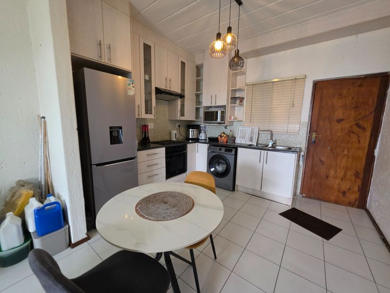 A functional kitchen featuring light-toned cabinetry, tiled flooring, integrated appliances, and a compact dining area, offering a practical layout for daily use.