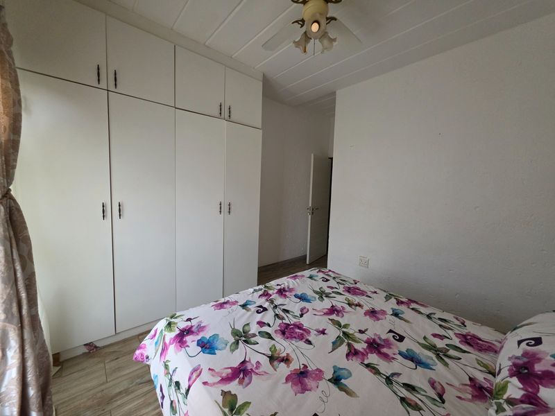 A bedroom featuring built-in white cupboards, a ceiling fan, and wood-look laminate flooring.