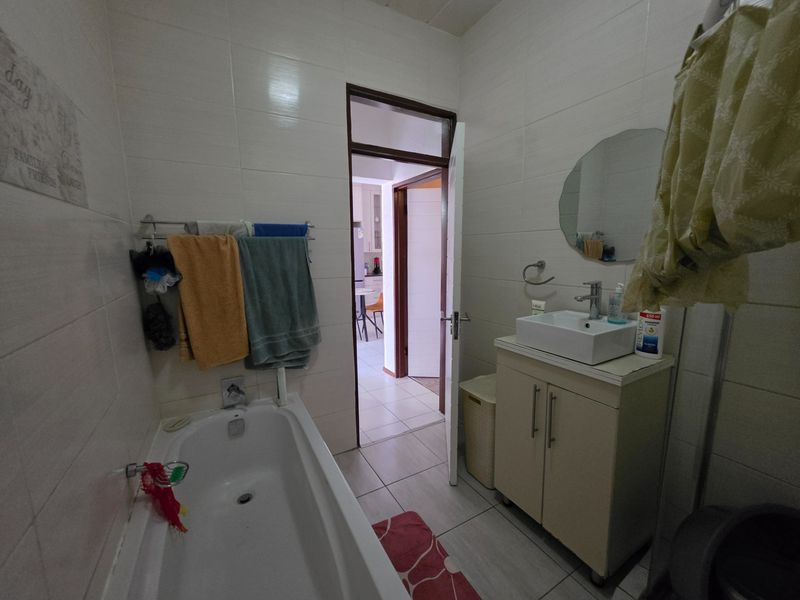 A functional bathroom featuring a built-in bathtub, a modern vessel sink with a vanity cabinet, and neutral wall and floor tiling.