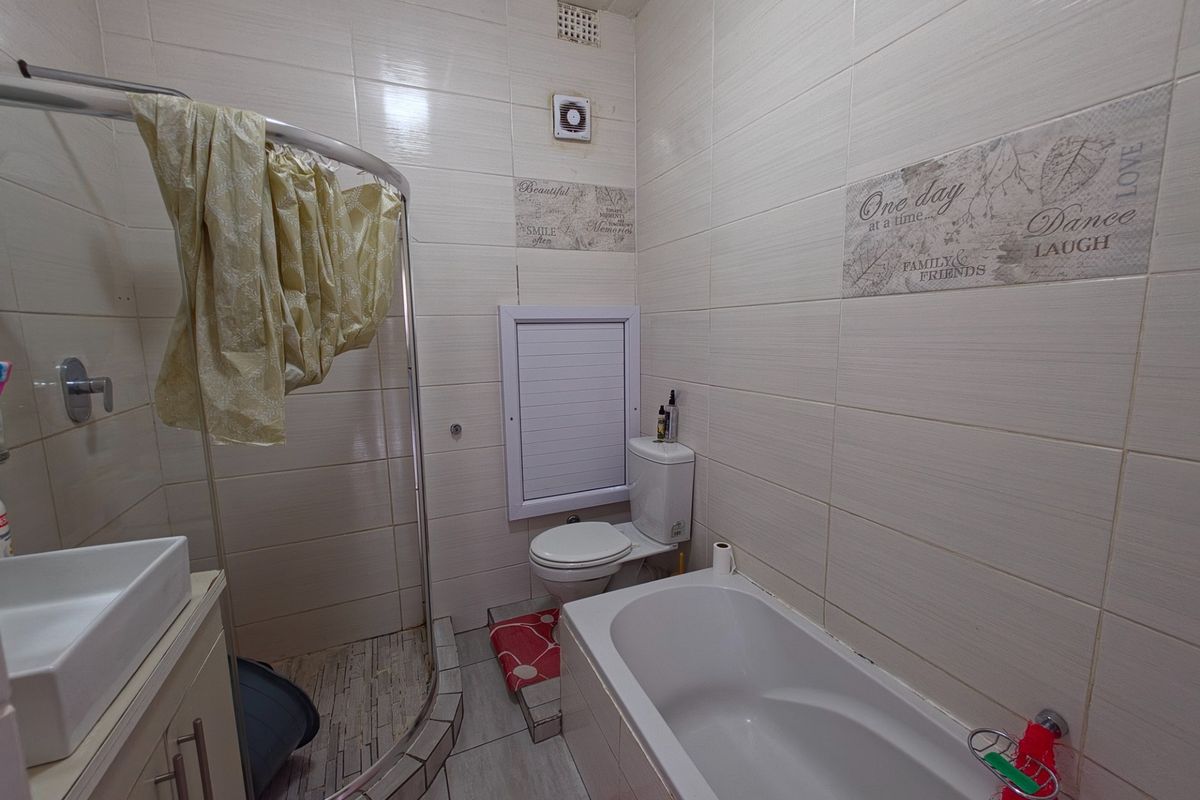 A compact bathroom featuring a shower enclosure, bathtub, toilet, and vanity basin with tiled wall finishes.