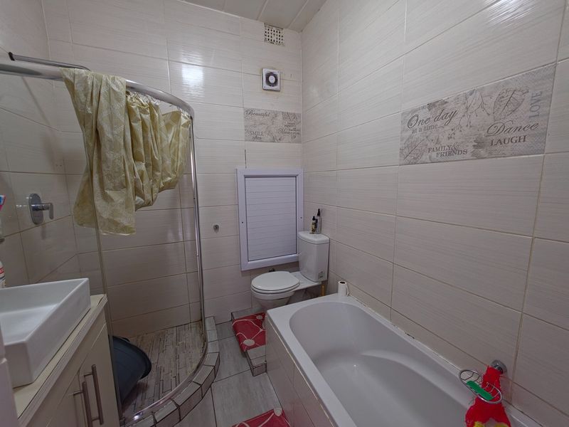 A compact bathroom featuring a shower enclosure, bathtub, toilet, and vanity basin with tiled wall finishes.