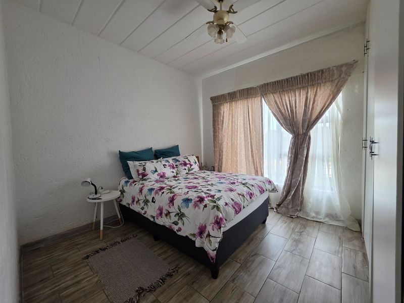 A bedroom featuring tiled flooring, built-in cupboards, and a ceiling fan, offering a functional space with natural light through large window treatments.