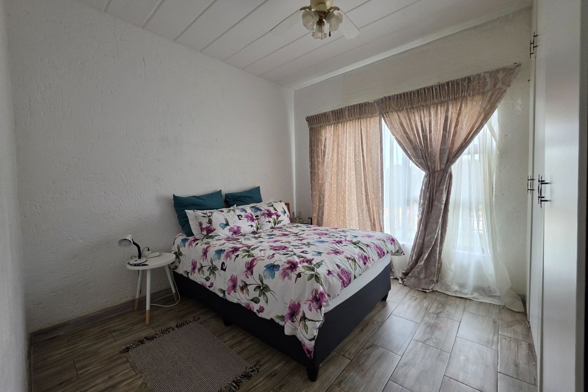 A bedroom featuring tiled flooring, built-in cupboards, and a ceiling fan, offering a functional space with natural light through large window treatments.