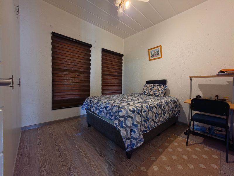 A functional bedroom featuring laminate flooring, built-in cupboards, and dual roller blinds, providing a practical space with potential for cosmetic updates.