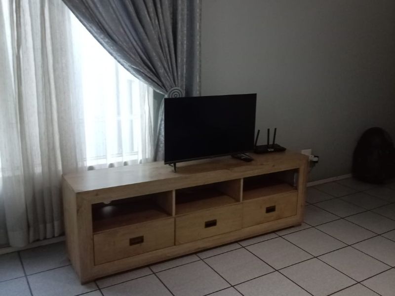 A living room area featuring neutral tiled flooring and a window with curtains.
