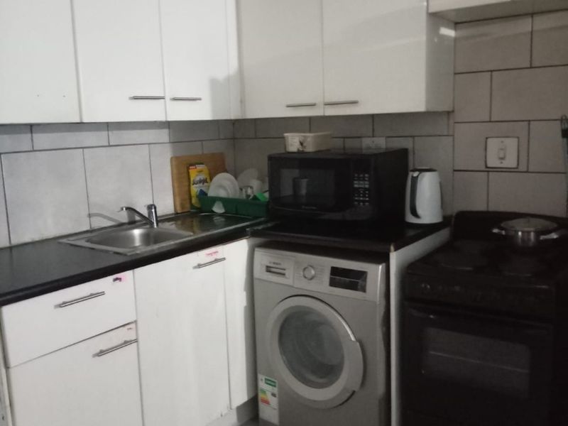 Compact kitchen featuring white cabinetry, dark countertops, tiled backsplash, and integrated space for a washing machine and electric stove.