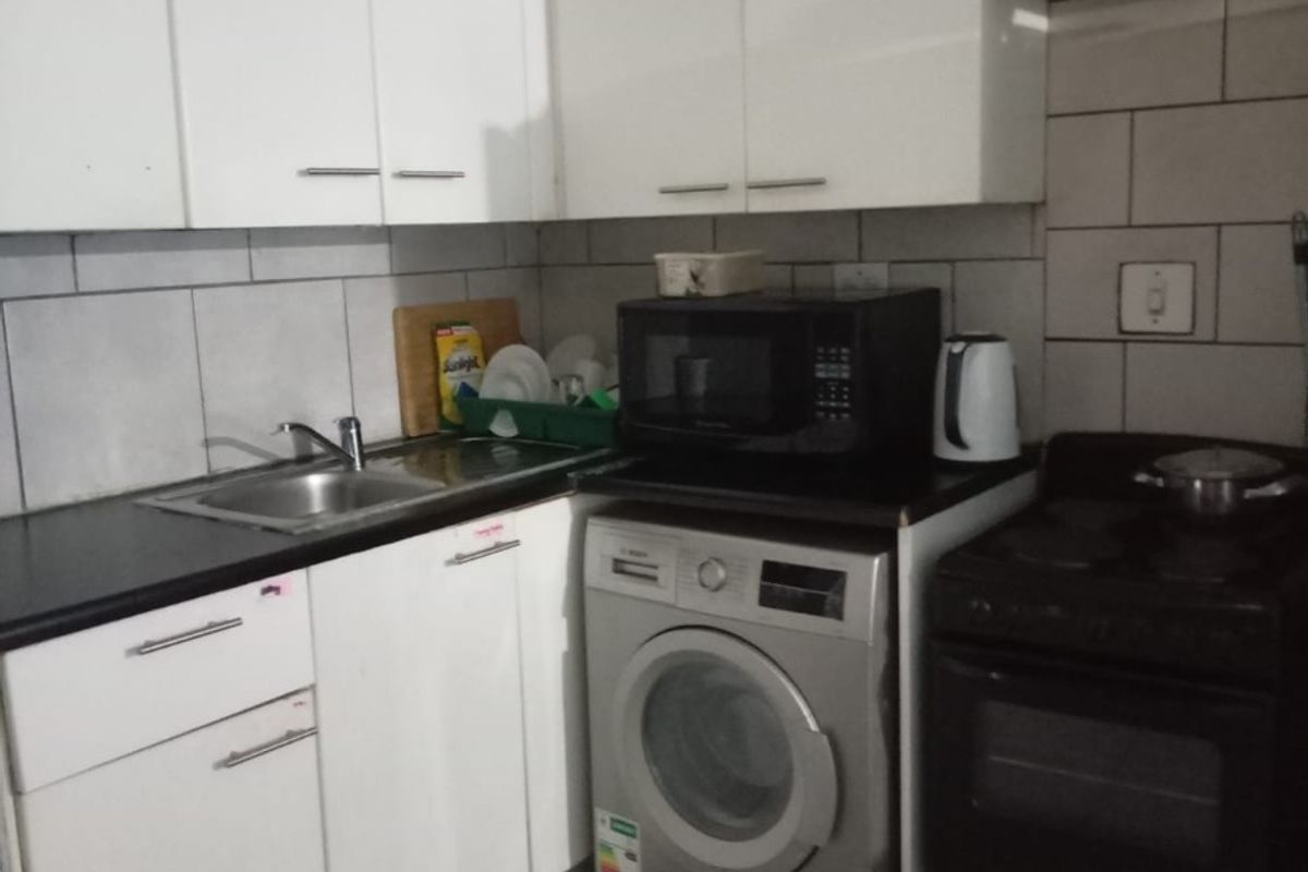 Compact kitchen featuring white cabinetry, dark countertops, tiled backsplash, and integrated space for a washing machine and electric stove.