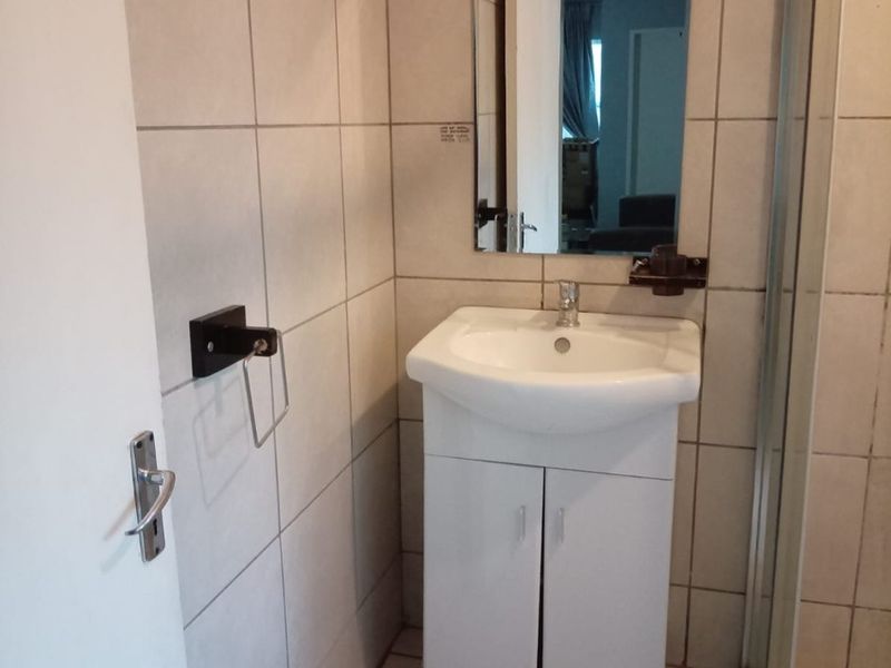 A compact bathroom featuring a white vanity cabinet with a basin, wall-mounted mirror, and a tiled shower enclosure.