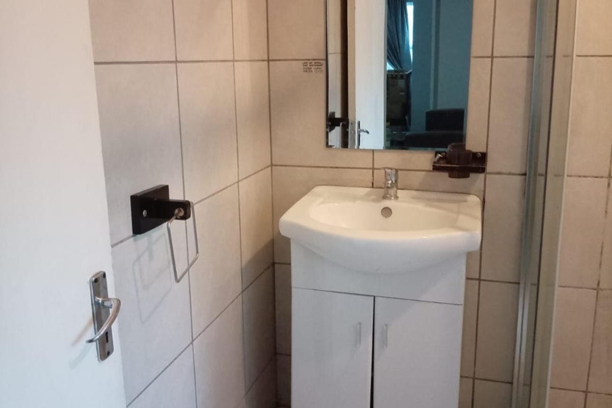 A compact bathroom featuring a white vanity cabinet with a basin, wall-mounted mirror, and a tiled shower enclosure.