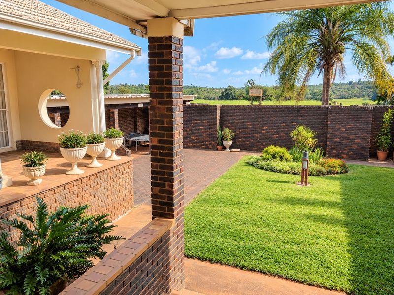 A well-maintained covered brick patio overlooking a landscaped garden and lawn, featuring a secure brick boundary wall and pleasant rural views.