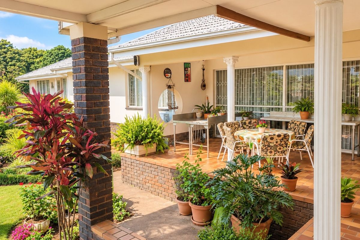A spacious covered patio featuring brick columns, tiled flooring, and built-in prep counters, overlooking a well-maintained garden area.