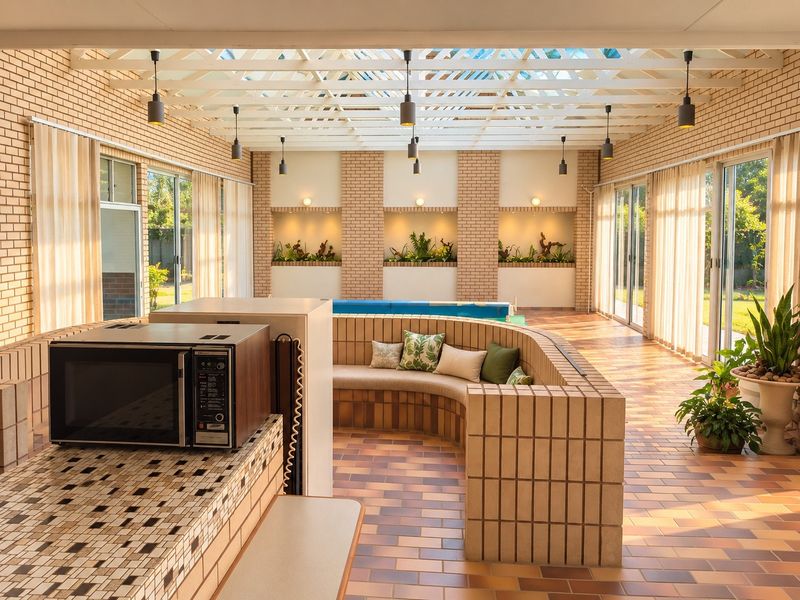 A spacious indoor pool area featuring brick masonry, a large skylight roof, built-in brick seating, and recessed wall niches, creating a bright and unique entertainment space.