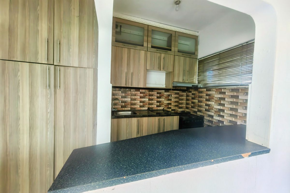 Compact kitchen featuring wood-look cabinetry, stone countertops, a breakfast bar, and a tiled backsplash, offering a functional layout for meal preparation.