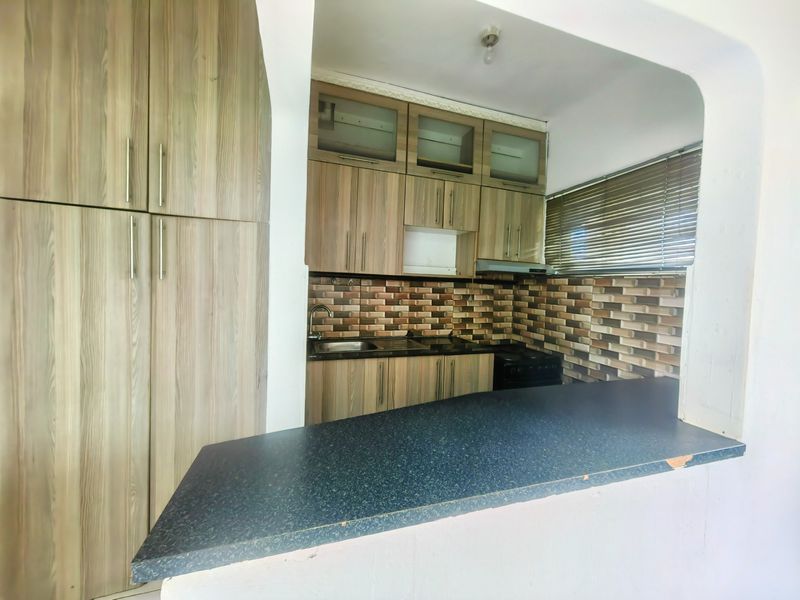 Compact kitchen featuring wood-look cabinetry, stone countertops, a breakfast bar, and a tiled backsplash, offering a functional layout for meal preparation.