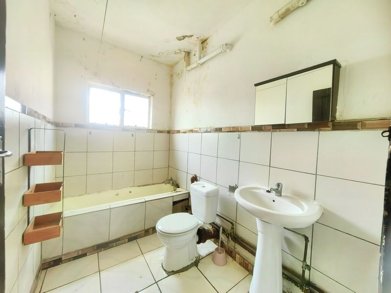 A dated bathroom featuring a bathtub, pedestal basin, and toilet, requiring significant renovation due to visible ceiling damage and exposed plumbing.
