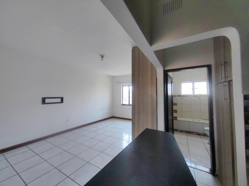 An open-plan living area featuring tiled flooring and a view into an adjacent bathroom, offering a blank canvas for interior design.