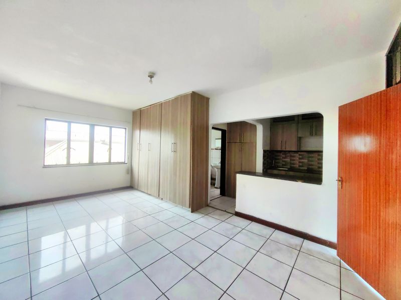 Open plan living area featuring tiled flooring, built-in cupboards, and a compact kitchen nook with cabinetry and counter space.