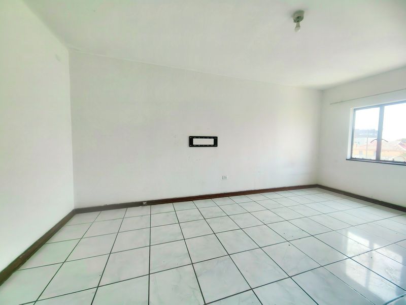 An empty living room featuring white walls, tiled flooring, and a wall-mounted TV bracket, offering a blank canvas for personalization.