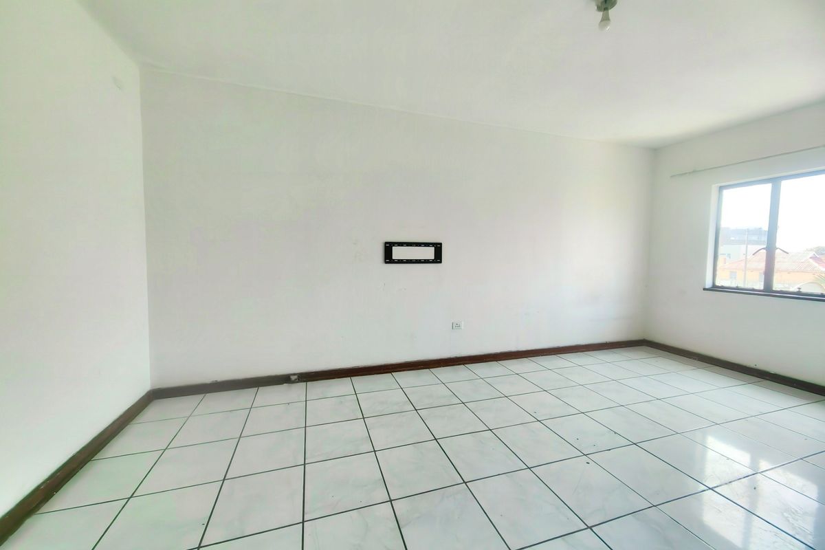 An empty living room featuring white walls, tiled flooring, and a wall-mounted TV bracket, offering a blank canvas for personalization.