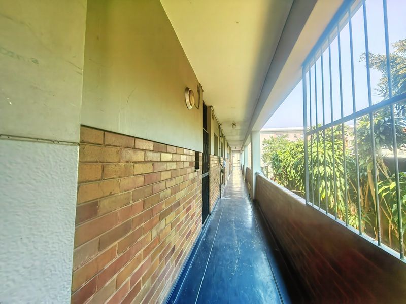 An exterior-facing hallway featuring exposed brickwork, security bars, and a paved walkway.