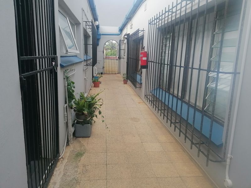 An outdoor walkway or corridor featuring tiled flooring, security gates, and protective window bars, providing access between apartment units.