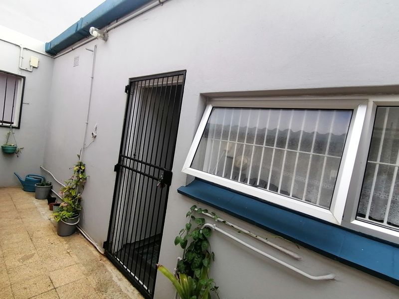 A rear exterior courtyard area featuring a security gate, awning windows with security bars, and tiled flooring.