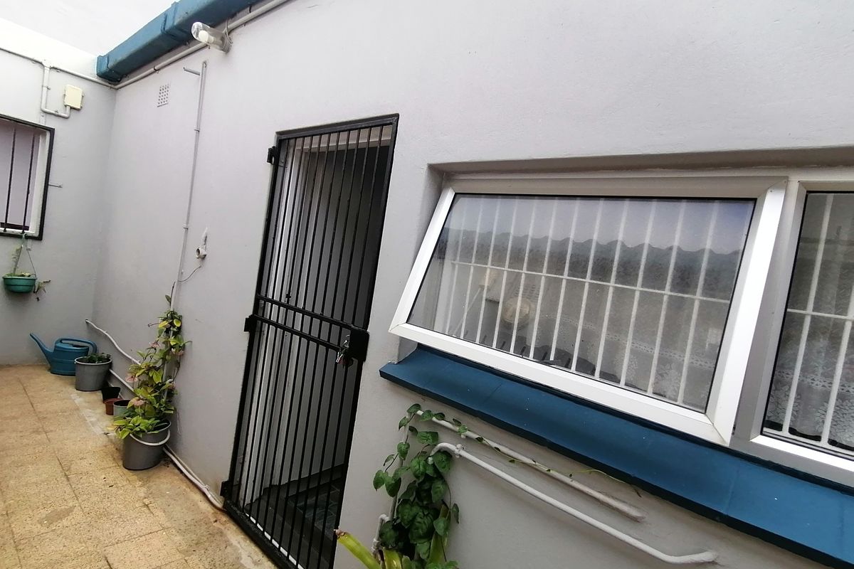 A rear exterior courtyard area featuring a security gate, awning windows with security bars, and tiled flooring.