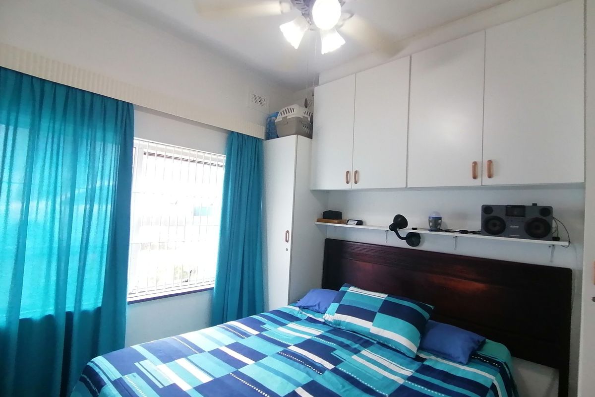 A bedroom featuring built-in overhead cupboards, a ceiling fan, and a window fitted with security bars.