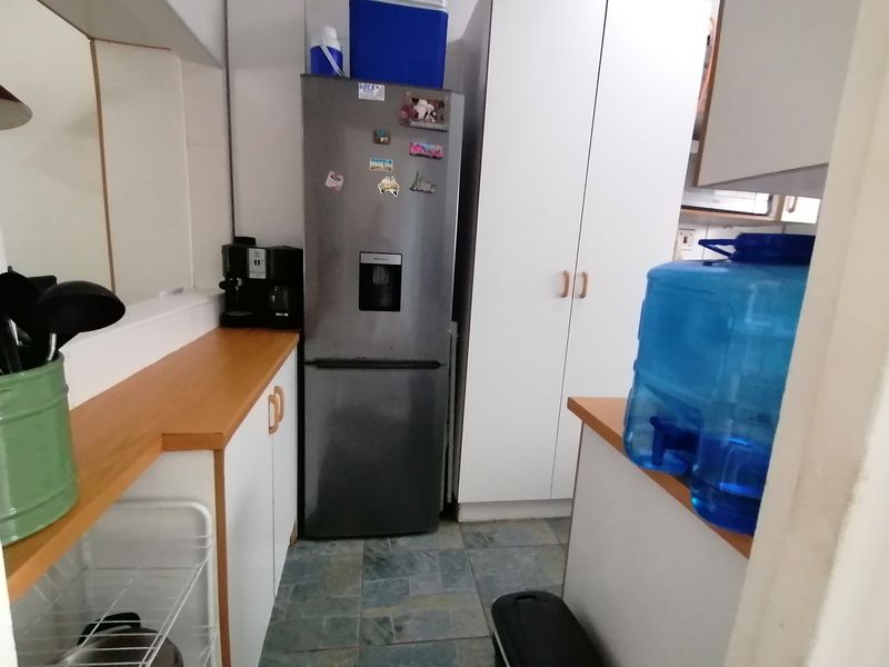 A compact kitchen area featuring white built-in cabinetry, laminate countertops, and tiled flooring, providing functional storage and workspace.