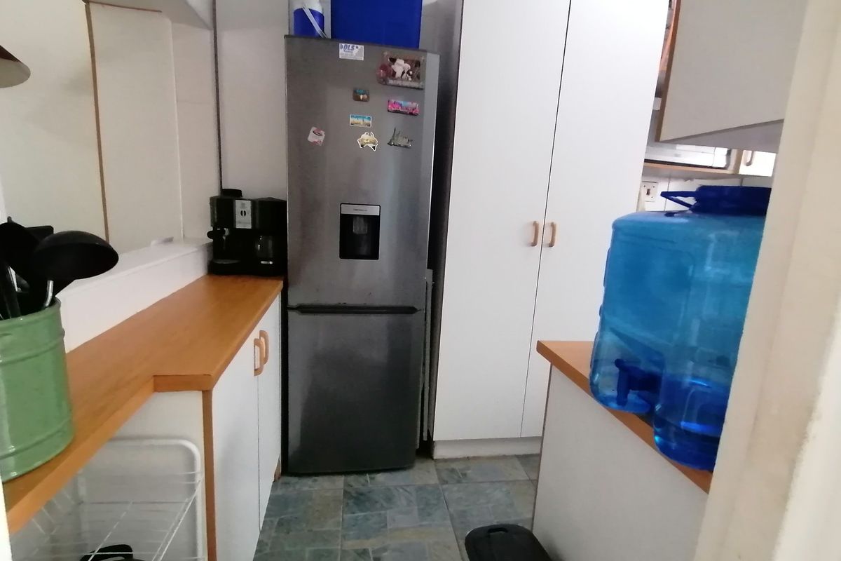 A compact kitchen area featuring white built-in cabinetry, laminate countertops, and tiled flooring, providing functional storage and workspace.