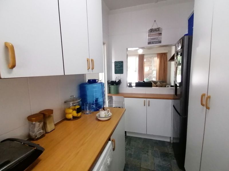 A functional kitchen featuring white cabinetry, wood-look laminate countertops, tiled flooring, and a convenient pass-through window connecting to the living area.