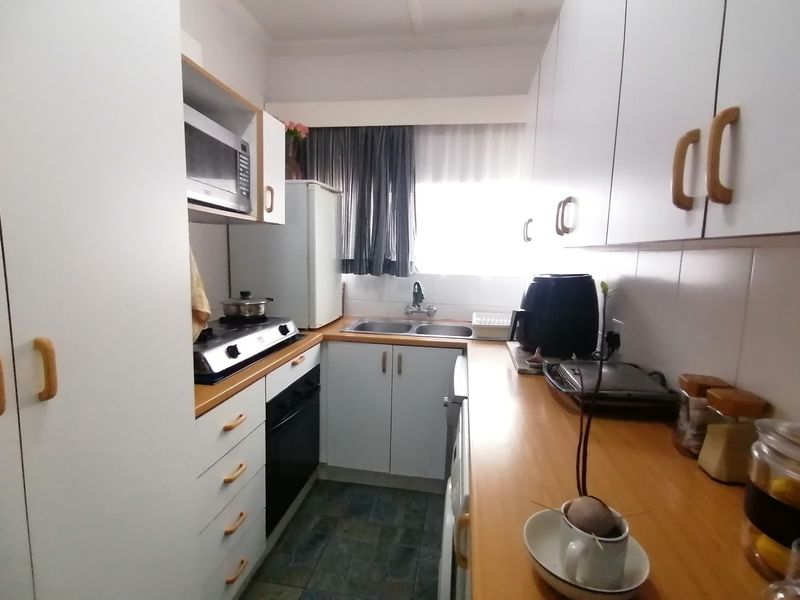 A compact galley-style kitchen featuring white cabinetry, wood-look laminate countertops, a built-in oven, gas hob, and a stainless steel double sink.