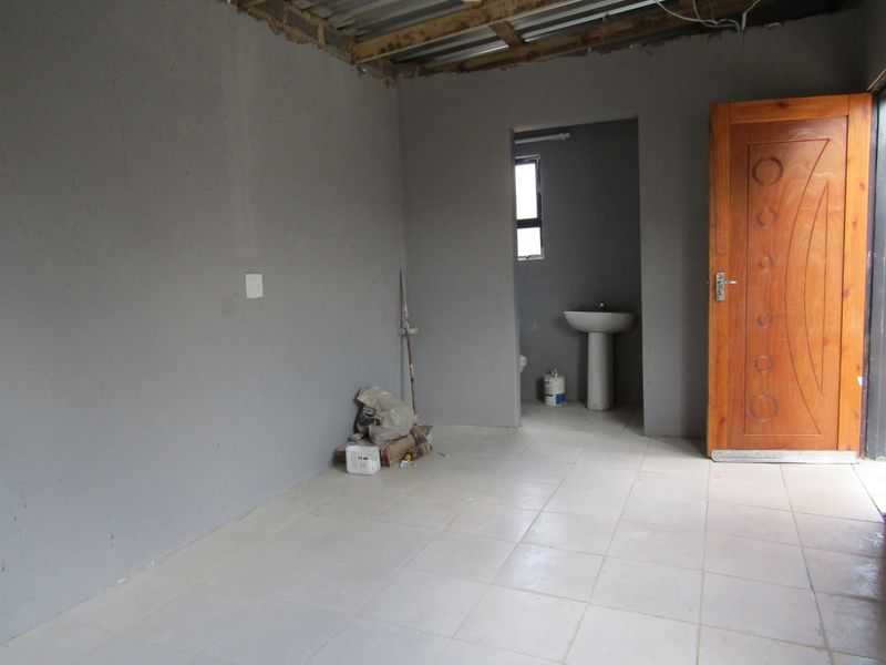 An unfinished bedroom space featuring tiled flooring, a pedestal basin in the en-suite area, and an exposed roof structure.