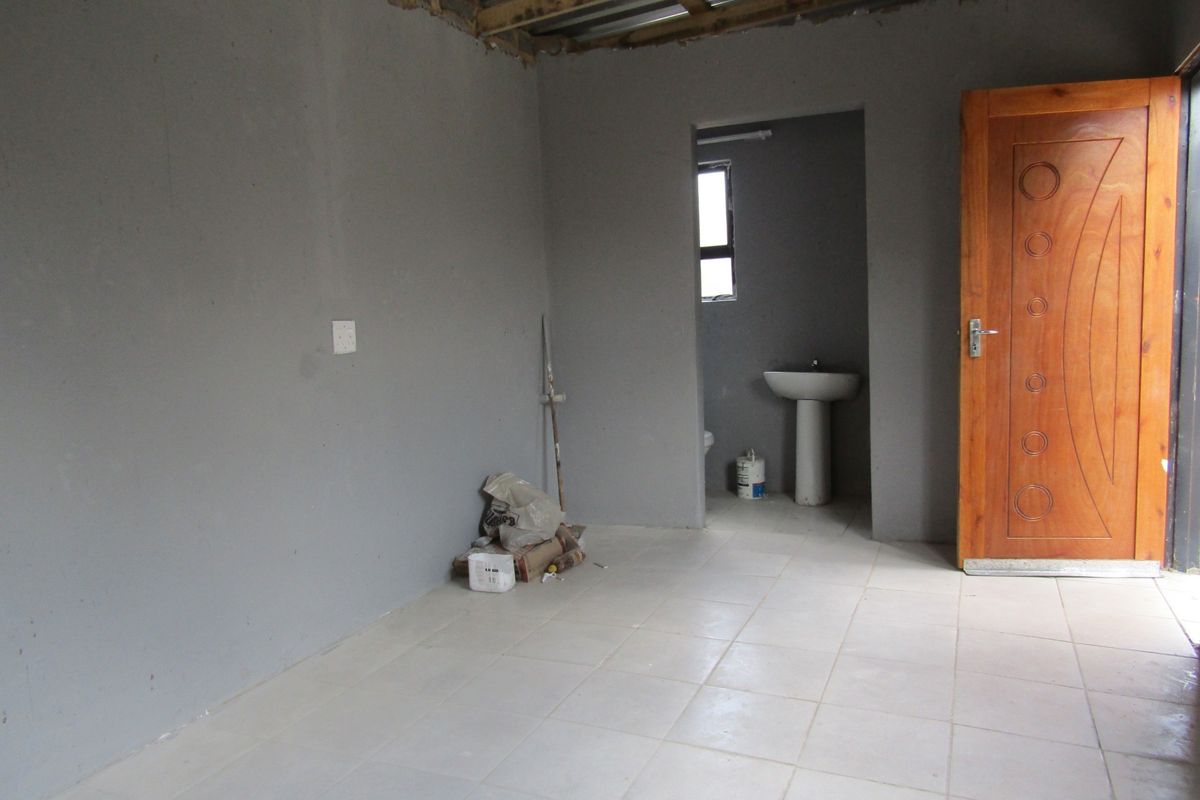 An unfinished bedroom space featuring tiled flooring, a pedestal basin in the en-suite area, and an exposed roof structure.