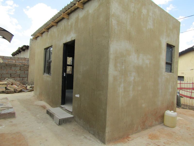A small, detached structure featuring cement rendered walls, a corrugated metal roof, and aluminium window frames, currently in an unfinished state.