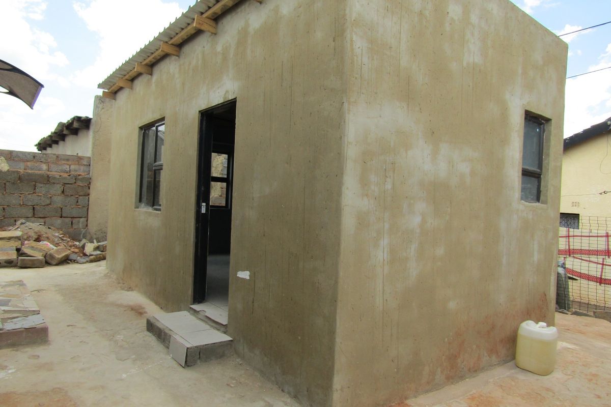 A small, detached structure featuring cement rendered walls, a corrugated metal roof, and aluminium window frames, currently in an unfinished state.