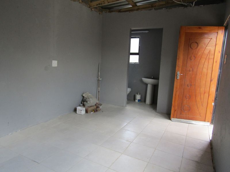 An unfinished bedroom space featuring tiled flooring, an en-suite bathroom area with a pedestal basin and toilet, and exposed ceiling rafters.