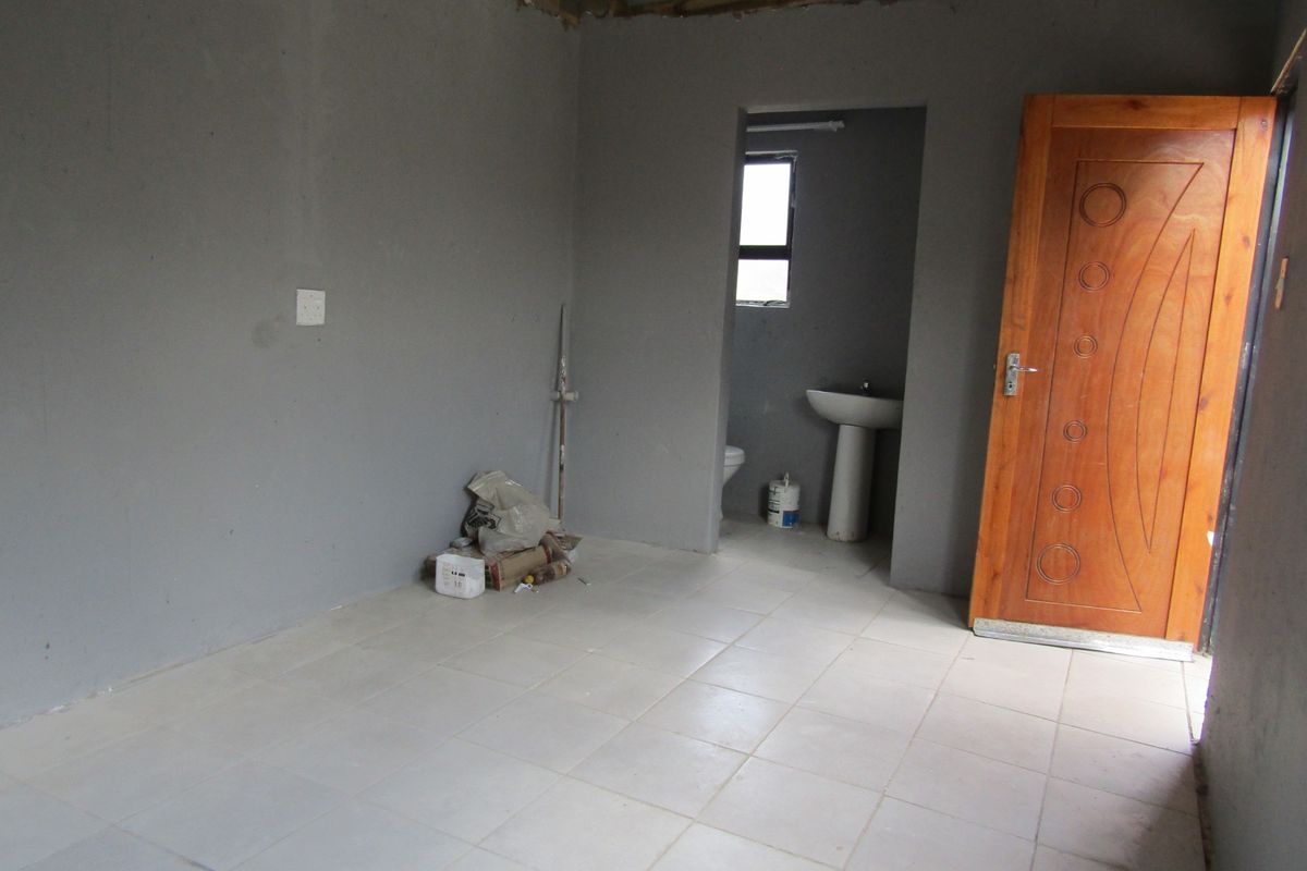 An unfinished bedroom space featuring tiled flooring, an en-suite bathroom area with a pedestal basin and toilet, and exposed ceiling rafters.