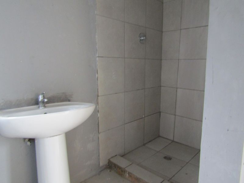 A basic bathroom featuring a pedestal basin and a tiled shower cubicle, currently in an unfinished state requiring cosmetic completion.