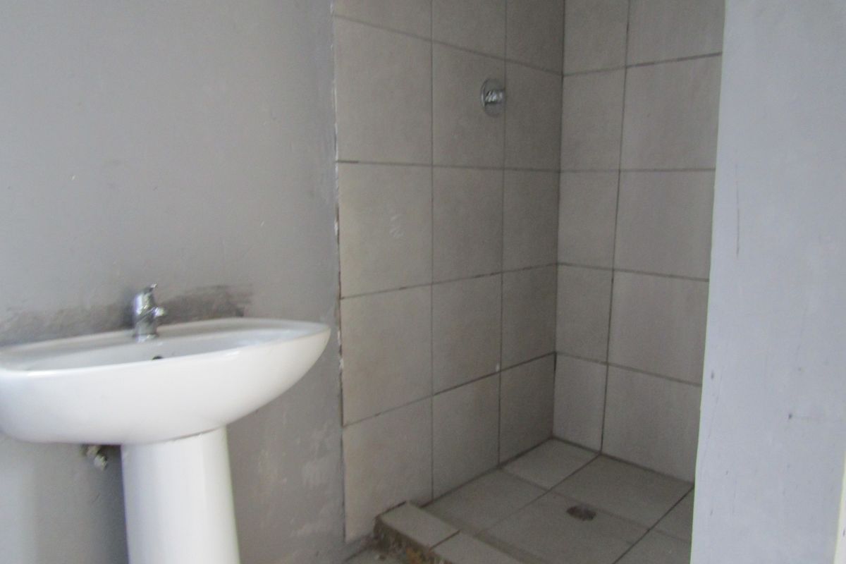 A basic bathroom featuring a pedestal basin and a tiled shower cubicle, currently in an unfinished state requiring cosmetic completion.