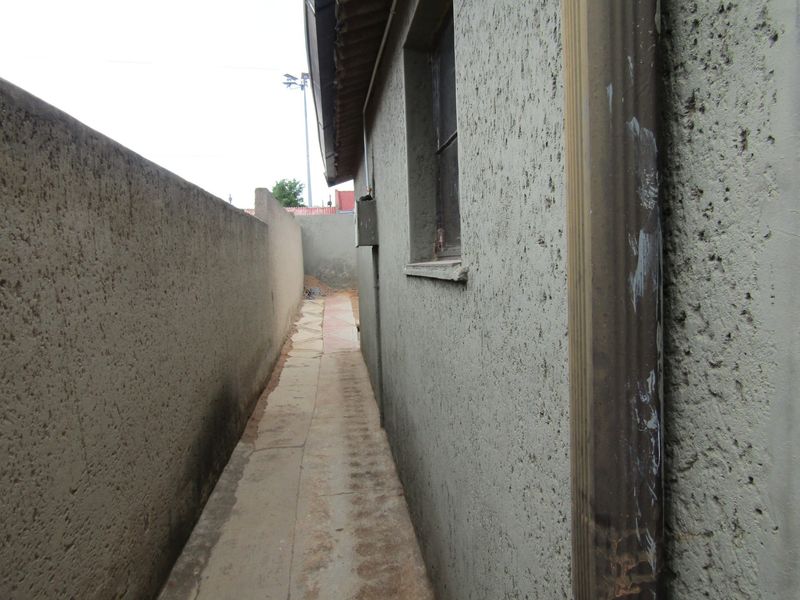 A narrow side passage featuring a paved walkway between the main building structure and a high boundary wall.